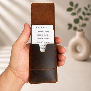以下が含まれることがあります： 茶色の革製カードケース。縦型のデザインで、白いクレジットカードを複数枚収納。カードケースは開いており、「CREDIT CARD」と書かれたカードが見える。革は使い古したような風合い。