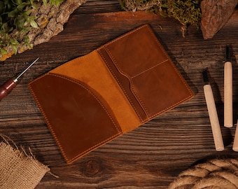 May include: A brown leather passport holder with multiple pockets and a flap closure. The holder is open and lying on a wooden surface.