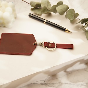 May include: A red leather key chain with a gold metal ring and a small leather tag. The tag has a stitched edge.