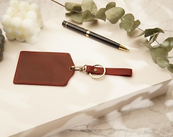 May include: A red leather key chain with a gold metal ring and a small leather tag. The tag has a stitched edge.