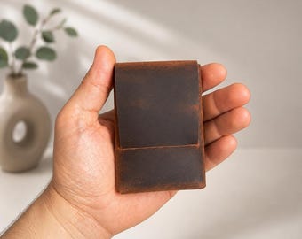 May include: A brown leather wallet with a distressed finish. The wallet is rectangular and appears to be folded over. The leather has a worn appearance, with variations in color. The wallet is held in a hand.