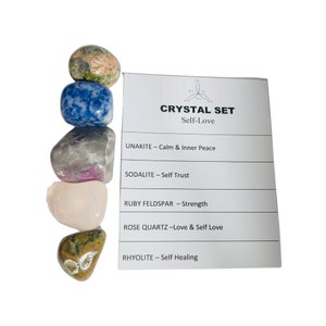 Peut inclure: Un ensemble de six cristaux roulés pour l'amour de soi, comprenant de l'unakite, de la sodalite, du feldspath rubis, du quartz rose et de la rhyolite. Les cristaux sont disposés en pile sur une carte blanche avec le nom de chaque cristal et sa signification associée.