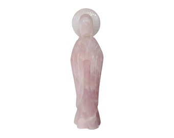 May include: A pink rose quartz statue of a woman with a halo. The statue is carved in a standing pose with hands clasped in prayer.