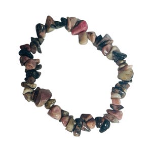 May include: A bracelet made of small, irregularly shaped stones in shades of pink, brown, black, and beige. The stones are strung together to form a circular shape. The bracelet is set against a white background.