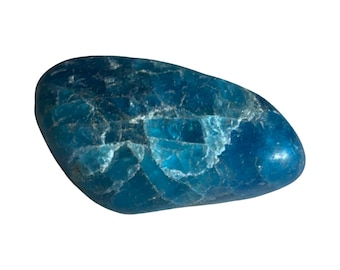 Puede incluir: Una piedra preciosa azul pulida, de forma ovalada, con una mezcla de tonos azul oscuro y claro. La piedra tiene una superficie lisa y brillante con estructuras cristalinas internas visibles. La apariencia general es un color profundo, similar al océano.