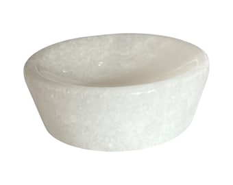 May include: A small, round, white stone bowl with a smooth, polished interior and a textured, crystalline exterior surface. The vessel features a wide, shallow basin and thick, tapered walls, showcasing the natural, translucent white mineral composition.