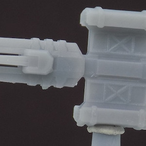 May include: A gray plastic model of a futuristic weapon with a long barrel and a complex design. The weapon has a series of ridges and grooves along the barrel and a rectangular box-like section in the middle.