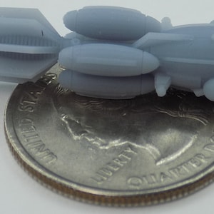 May include: A gray, 3D printed model of a small spaceship with a rocket engine and three booster rockets. The spaceship is about the size of a US quarter.