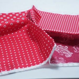 May include: A folded red pocket square with four distinct patterns: white polka dots, small white floral designs, a white grid, and a paisley print. The edges are finished with a white border.