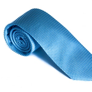 Puede incluir: Una corbata de seda azul con estampado enrollada. La corbata es de color azul claro con un estampado blanco.