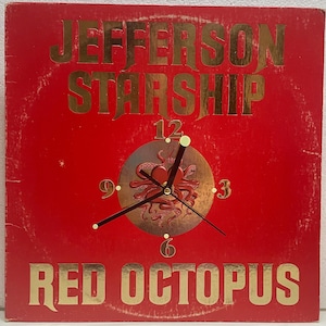 May include: A red square clock with gold lettering that reads "JEFFERSON STARSHIP" and "RED OCTOPUS". The clock face features a gold and brown octopus design with black clock hands and numbers.