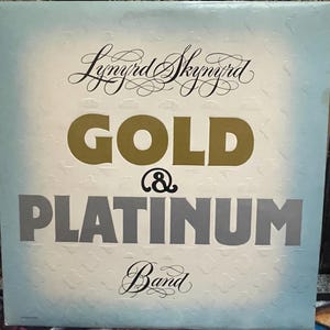 May include: Album cover for Lynyrd Skynyrd's "Gold & Platinum" album. The album title is in large gold and gray letters. The band's name is in elegant script at the top, with the word "Band" at the bottom.