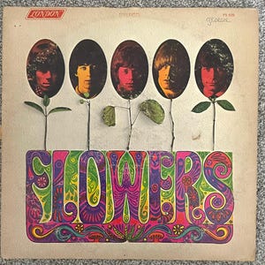 May include: A vintage vinyl record cover titled Flowers by The Rolling Stones. The cover features five oval portraits of band members atop thin stems with green leaves, set against a beige background with colorful, psychedelic lettering.