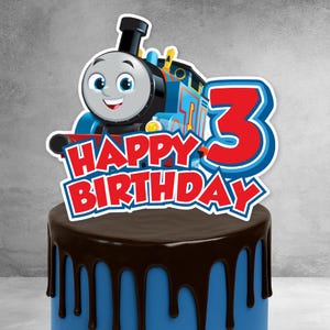 May include: A cake topper with a cartoon train design, the words "HAPPY BIRTHDAY", and the number "3". The train is blue, black, and white, and the number is red with a blue outline. The cake has blue icing with chocolate dripping down the sides.