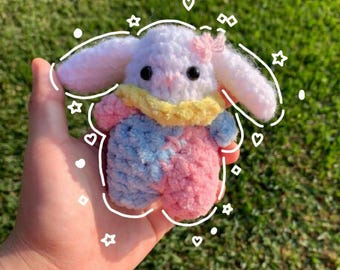 May include: A crocheted bunny plush toy with white fur, blue and pink yarn, and a yellow scarf. The bunny has a pink bow on its head.