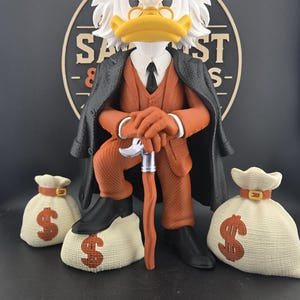 Könnte beinhalten: Eine stilisierte Entenfigur mit dunkelgrauer Schiebermütze, schwarzem Mantel und orangefarbenem Anzug mit schwarzer Krawatte. Die Figur hält einen Gehstock mit silbernem Knauf, steht auf einem weißen Geldsack mit Dollarzeichen und zwei weiteren.