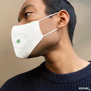 Puede incluir: Una mascarilla facial blanca con un asterisco verde en la parte delantera. La mascarilla la lleva puesta una persona.