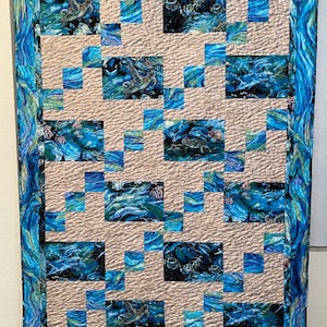 May include: A beige and blue quilt with a repeating pattern of sea turtles, fish, and coral. The quilt is quilted with a wavy pattern.