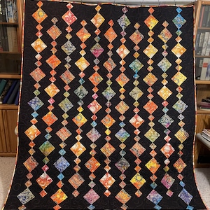 May include: A black quilt with a diamond pattern. Each diamond is filled with a different colorful fabric featuring a sun design. The quilt is edged with a red border.