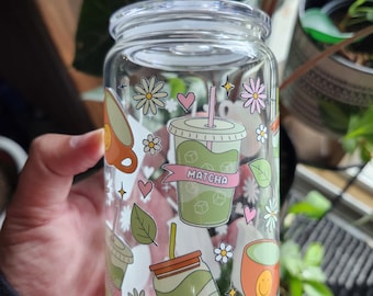May include: A clear glass tumbler with a lid, decorated with colorful illustrations of matcha drinks, daisies, hearts, and leaves. The word "Matcha" is on a banner. The tumbler is designed for cold beverages.