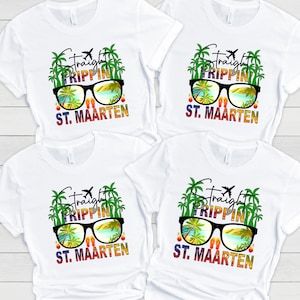 May include: Four white t-shirts with a colorful graphic design. The design features sunglasses reflecting a tropical beach scene, palm trees, and the words "Straight Trippin' St. Maarten". A small airplane graphic is also included.