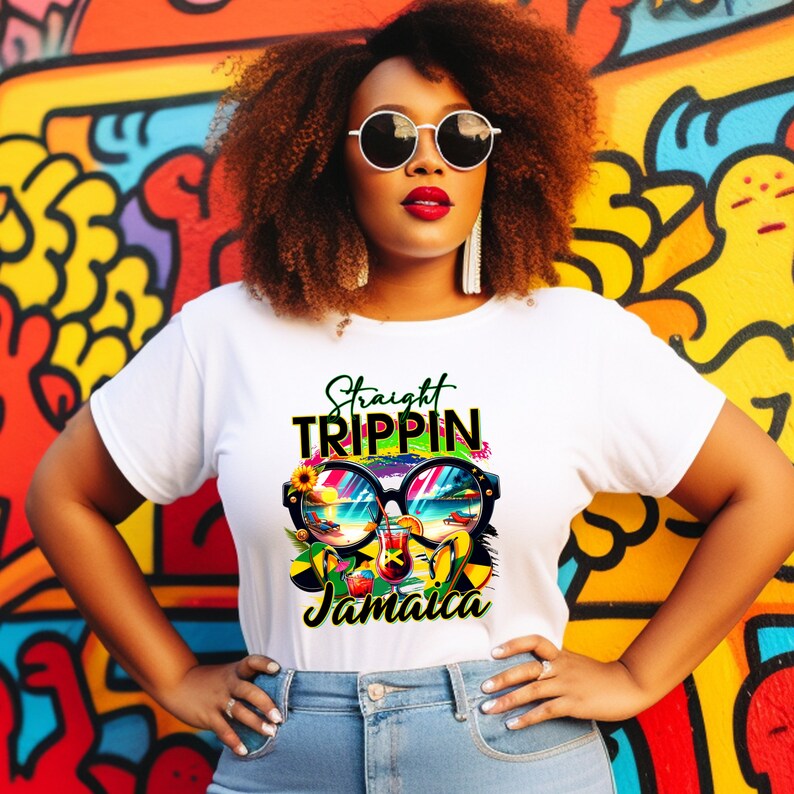 May include: White t-shirt with a colorful graphic design featuring sunglasses, a beach scene, and the words "Straight Trippin Jamaica." The design includes yellow, green, blue, and red elements. The shirt is worn by a person with curly brown hair and sunglasses.