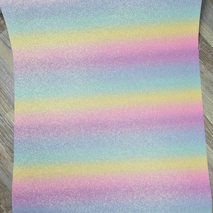 May include: A sheet of iridescent glitter fabric with a rainbow stripe pattern. The fabric has a light blue, yellow, pink, and purple color scheme.
