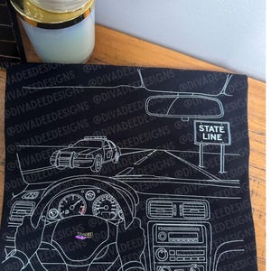May include: Black canvas art featuring a white line drawing of a car interior, including the steering wheel, dashboard, and a police car on the road. The words "STATE LINE" are visible on a sign.
