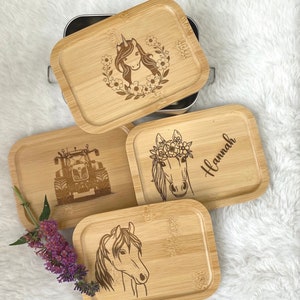 Könnte beinhalten: Eine Sammlung von Bambustabletts mit eingravierten Designs. Ein Tablett zeigt ein Einhorn, umgeben von Blumen, ein anderes einen Traktor, und zwei weitere zeigen Pferde. Ein Tablett ist mit dem Namen "Hannah" personalisiert. Die Tabletts sind rechteckig mit abgerundeten Ecken.