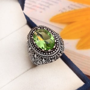May include: A silver ring with an oval-shaped green gemstone set in a detailed silver setting.