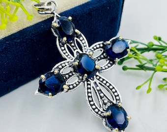 May include: A silver cross pendant with a filigree design and five blue gemstones. The pendant has a loop at the top for attaching to a chain.