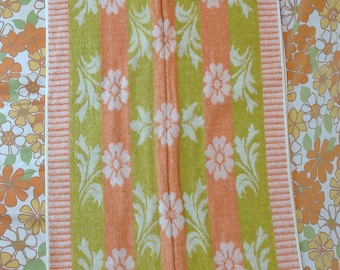 May include: Two hand towels with a striped pattern in shades of green, orange, and white. The towels have a floral design with white flowers and green leaves.