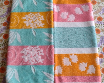 May include: Two hand towels with a striped pattern. One towel is turquoise with orange and pink stripes, the other is white with pink and orange stripes. Both towels have a floral design.