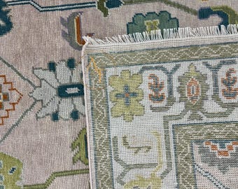 May include: Close-up of a beige rug with a detailed floral pattern in shades of green, brown, and white. The rug has a fringed edge.