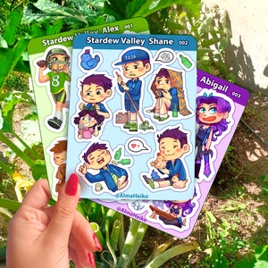 May include: Three sticker sheets featuring characters from the video game Stardew Valley. The first sheet features Alex, the second sheet features Shane, and the third sheet features Abigail. Each sheet has multiple stickers with different poses and expressions. The stickers are printed on glossy paper and have a vibrant color palette.