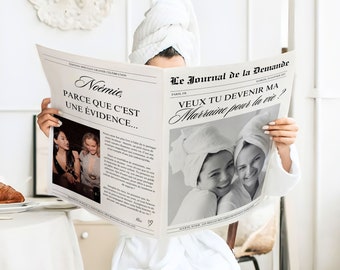 May include: A newspaper headline reads "Noémie, parce que c'est une évidence..." and "Le Journal de la Demande" with the text "Veux tu devenir ma marraine pour la vie?"  The newspaper is being held by a person in a white bathrobe.