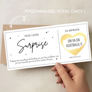 May include: A white card with black text that reads "Surprise" and "Pour Laura". The card has a gold scratch-off heart that says "On va en Australie!!" and "Gratte ici".