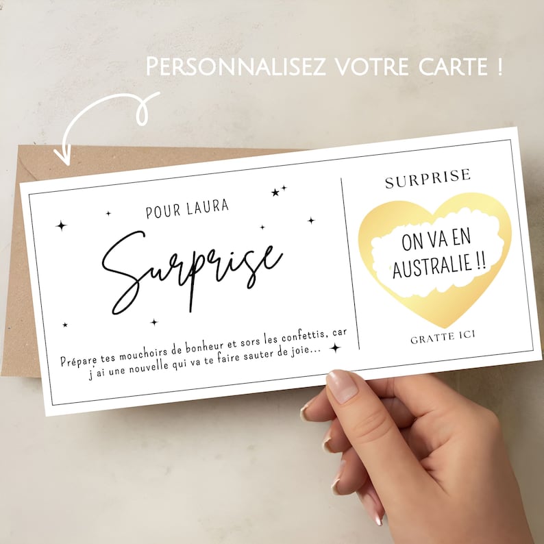 May include: A white card with black text that reads "Surprise" and "Pour Laura". The card has a gold scratch-off heart that says "On va en Australie!!" and "Gratte ici".