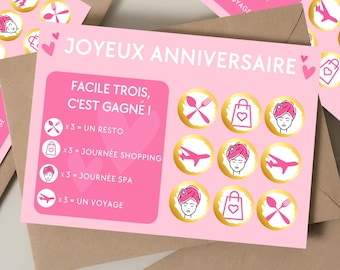 May include: Pink and gold card with the text "Joyeux Anniversaire" and "Facile Trois, C'est Gagné!"  The card has a game board with nine circles, each containing a different icon. The icons include a fork and knife, a shopping bag, a woman with a towel on her head, an airplane, and a heart.