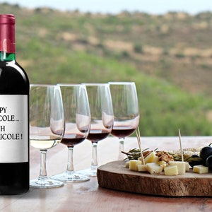 K&ouml;nnte beinhalten: Eine Flasche Rotwein mit einem Etikett, auf dem "Papy Picolo... Euh Bricole!" steht. Die Flasche steht auf einem Holztisch mit vier Weingl&auml;sern, einer K&auml;se- und Traubenplatte und einem verschwommenen Hintergrund aus sanften H&uuml;geln.