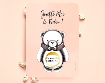 May include: A pink card with a black and white illustration of a bear wearing a bow tie. The bear has a gold circle on its belly with the text "Tu vas être COUSINE!" inside. The card also has the text "Gratte Moi le Bidou!" in black.