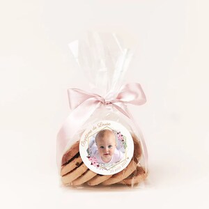 May include: A clear plastic bag filled with cookies and tied with a pink ribbon. A round sticker with a photo of a baby girl and the text "Bapteme de Louiza 20 ao&ucirc;t 2023" is attached to the bag.