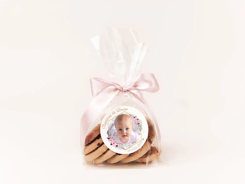 May include: A clear plastic bag filled with cookies and tied with a pink ribbon. A round sticker with a photo of a baby girl and the text "Bapteme de Louiza 20 ao&ucirc;t 2023" is attached to the bag.