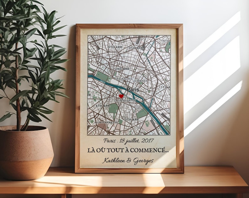 May include: Framed map print of Paris, France, with a red heart marking a location. The map is in neutral tones, with text indicating a date and names. The wooden frame adds a classic touch to the artwork.