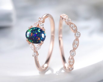 Könnte beinhalten: Ein Set aus zwei Ringen aus Roségold mit einem schwarzen Opal-Edelstein und Pavé-Diamanten. Der Verlobungsring hat einen großen ovalen schwarzen Opal, der von kleinen Diamanten umgeben ist. Der Ehering ist ein zartes Band mit einer Reihe kleiner Diamanten.