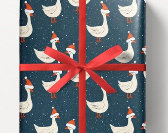 May include: Gift-wrapped present featuring wrapping paper with a pattern of white geese wearing Santa hats on a dark blue background with white snowflakes. The gift is tied with a red ribbon and bow. The text "https://www.etsy.com/shop/QuicklyBeeShop" is at the bottom.