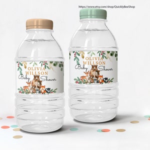 May include: Two clear plastic water bottles with labels that say "Olivia Willson Baby Shower" in gold lettering. The labels feature a watercolor illustration of a bear and other woodland animals.
