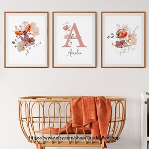 May include: Three framed prints with watercolor floral designs and ladybugs. The center print features the letter A in pink with the name Amelia below it.
