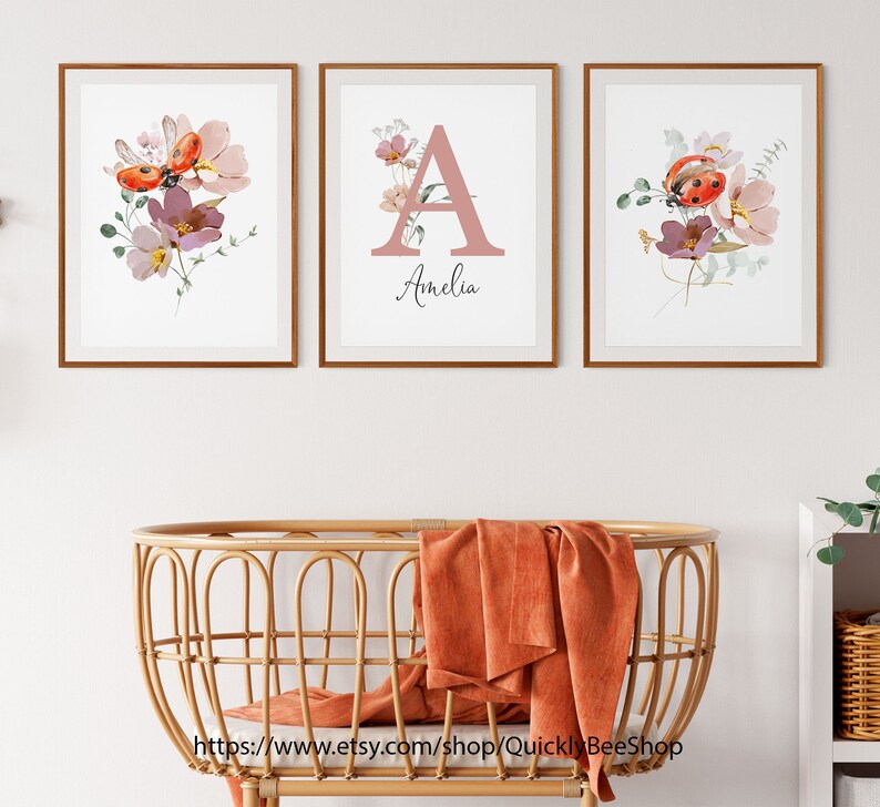 May include: Three framed prints with watercolor floral designs and ladybugs. The center print features the letter A in pink with the name Amelia below it.