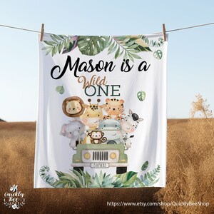 May include: White baby blanket featuring a green safari jeep and jungle animals. The text reads "Mason is a Wild One".